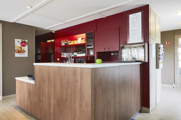 A modern bar area with a wooden counter and red accents, featuring a variety of bottles and glasses. - Campanile Arras - Saint Nicolas (Saint-Nicolas)