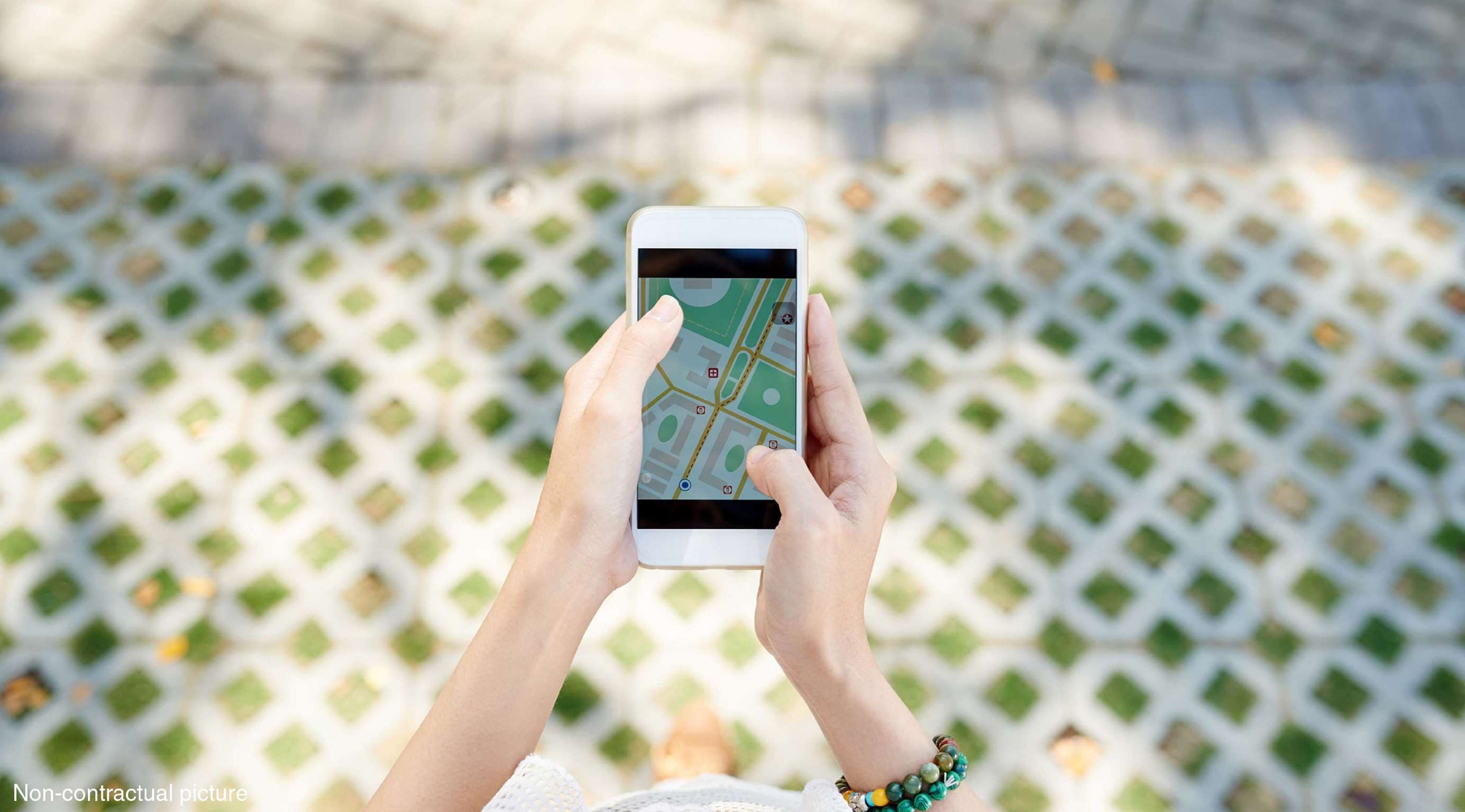 Pessoa segurando um smartphone com um mapa exibido, em pé sobre uma superfície estampada.