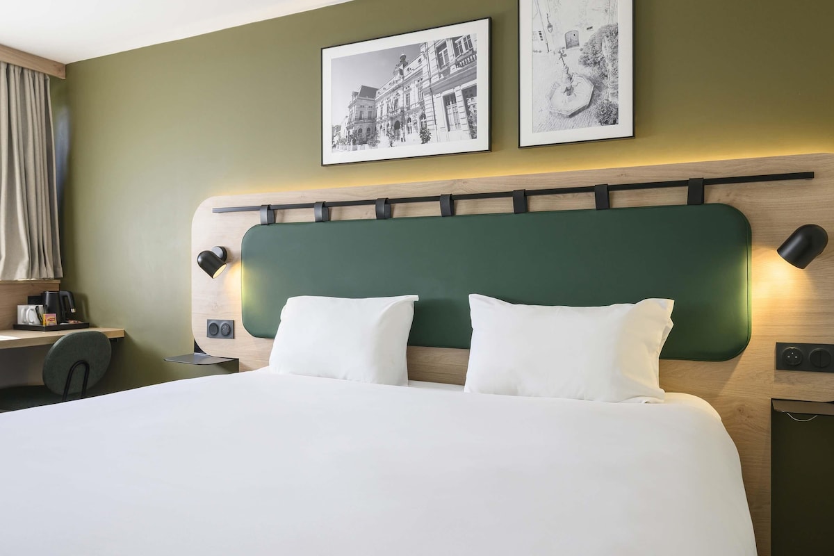 Habitación de hotel con cama, escritorio, silla y dos cuadros en la pared.
