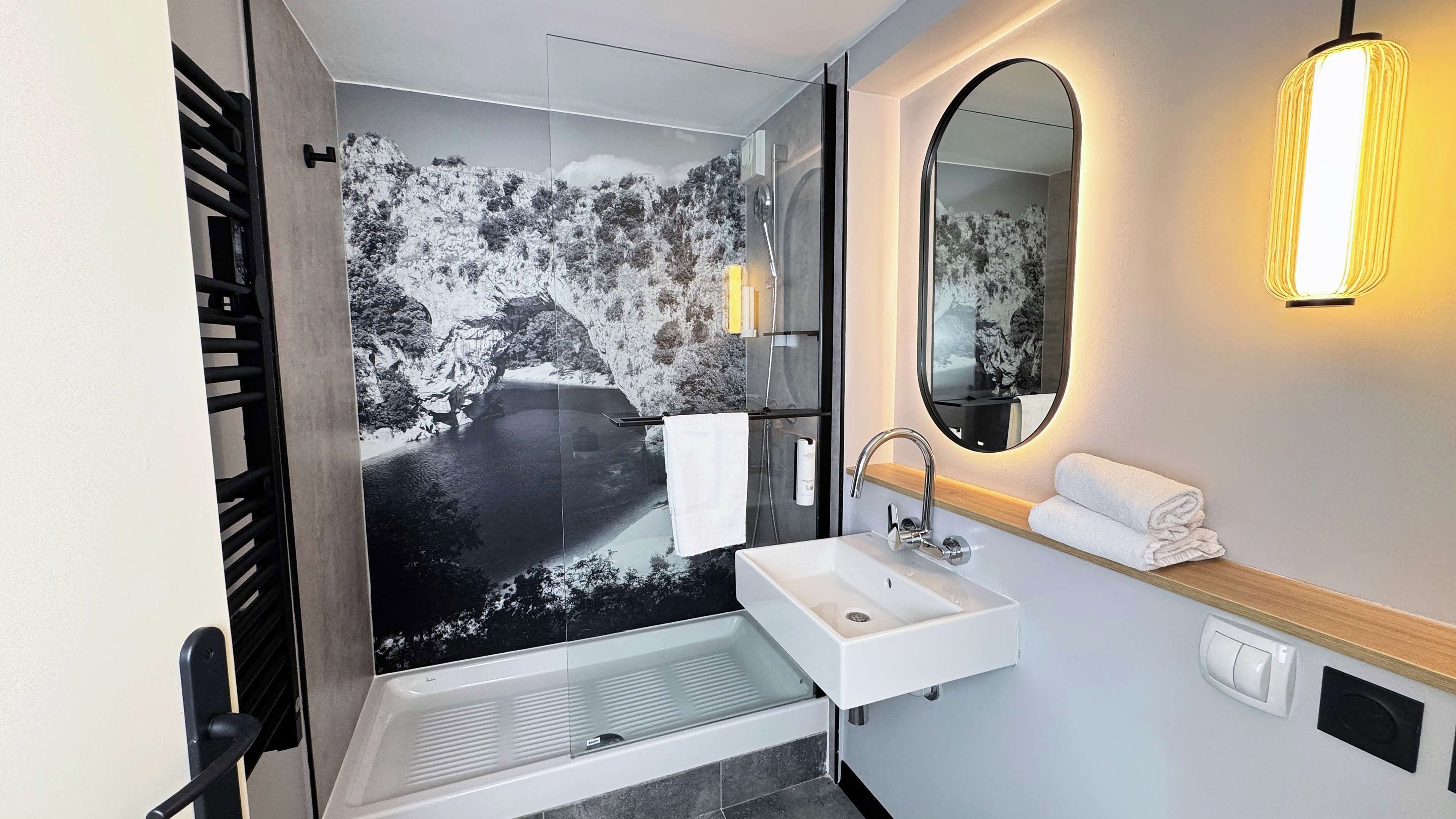 Un baño moderno con cabina de ducha de vidrio, lavamanos blanco y espejo con luz empotrada.