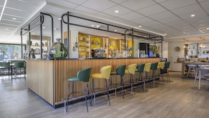 A modern bar area with a wooden counter, bar stools, and a coffee machine. - Campanile NATURE - Bollène (Bollene)