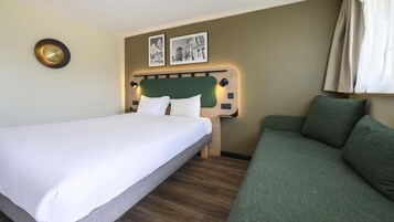Una habitación de hotel con una cama, un sofá verde, un cabecero con decoración en la pared y un reloj fijado a la pared.