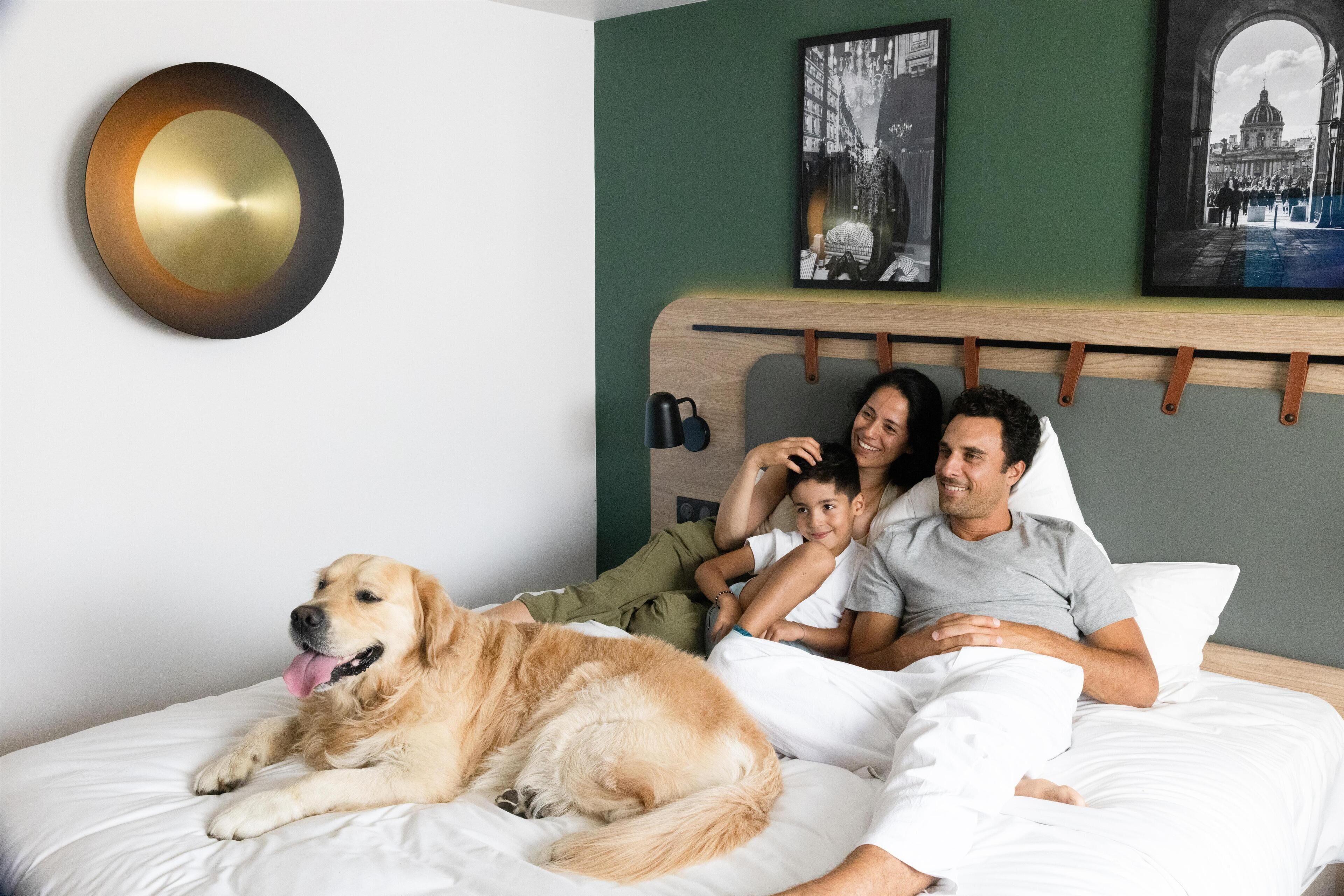 Un lit avec un grand chien, une famille de quatre personnes et un cadre photo accroché au mur.