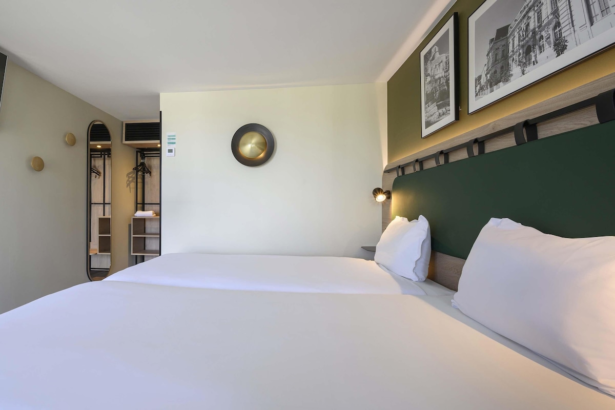 Una habitación de hotel con una cama, un reloj de pared, un espejo y un cuadro enmarcado.