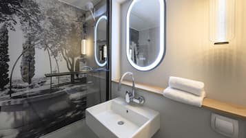 Un baño moderno con cabina de ducha de vidrio, un lavamanos blanco y dos espejos con iluminación integrada.
