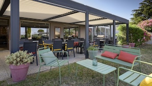 An outdoor patio area with tables and chairs, a covered seating area, and potted plants. - Campanile NATURE - Bollène (Bollene)