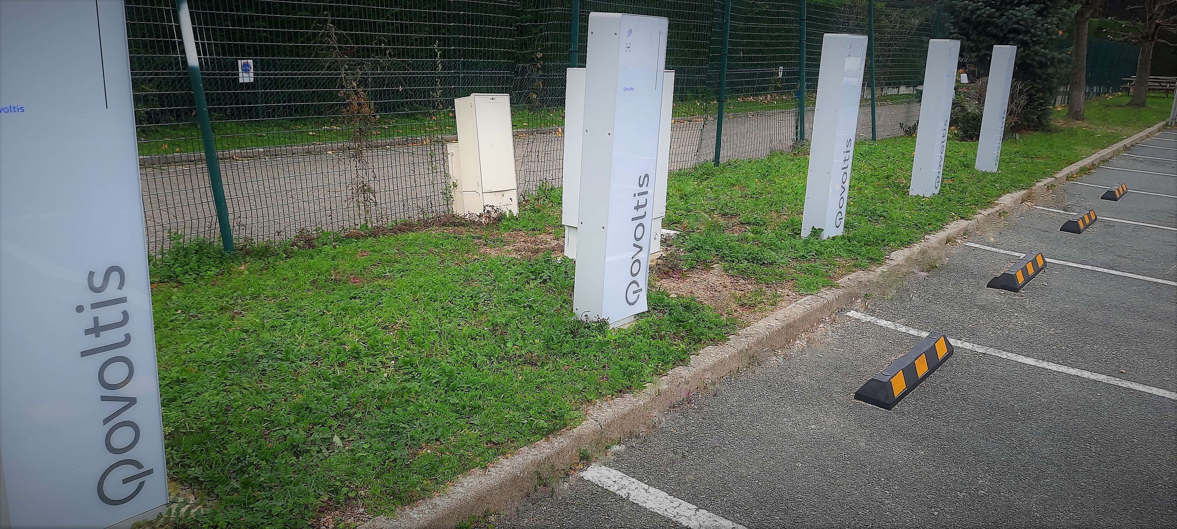 A parking area with a green fence and a grassy area beside it.