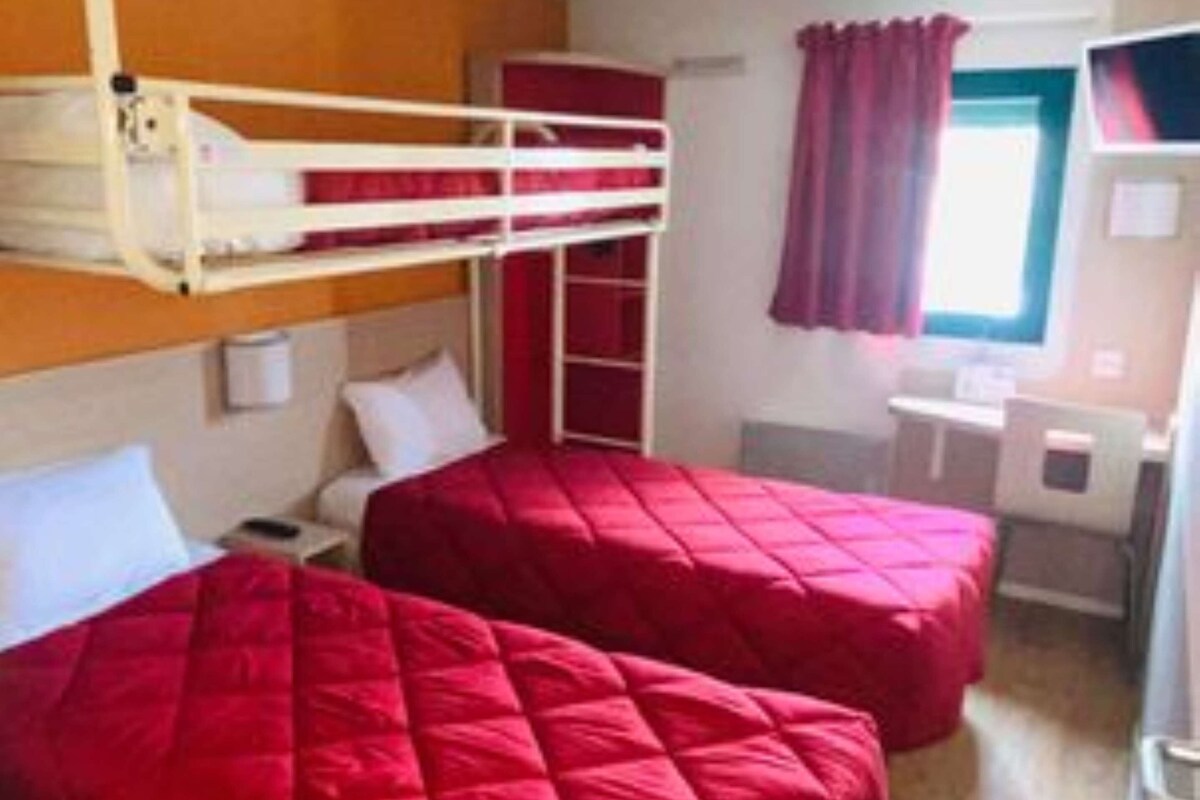 Una habitación con dos camas, una litera, un escritorio, una silla y una ventana con cortinas.