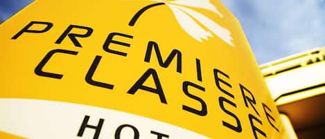 Una señal amarilla con la inscripción 'PREMIERE CLASSE HOTELS' y un símbolo blanco de fleur-de-lis.
