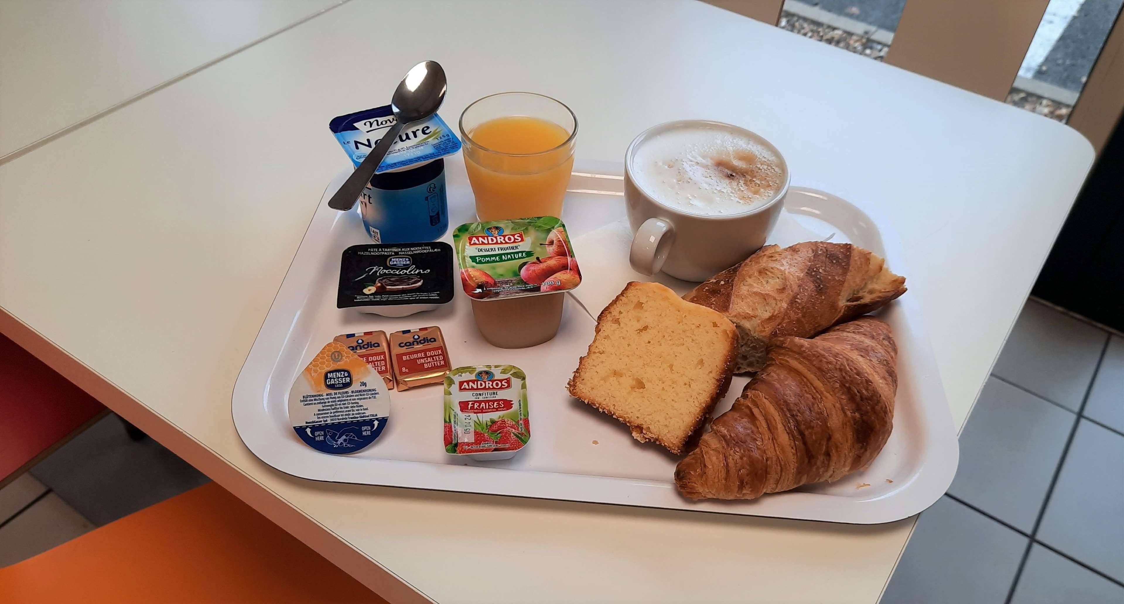 A breakfast tray with a croissant, juice, coffee, and various yogurt containers.