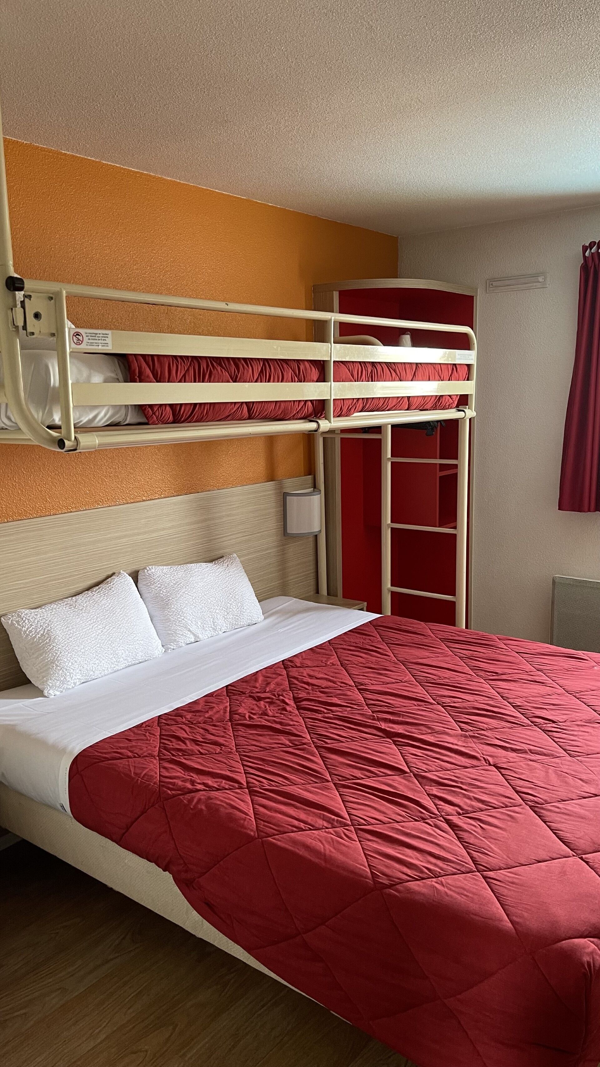 Habitación con literas, un edredón acolchado rojo, almohadas blancas y un cabecero de madera.