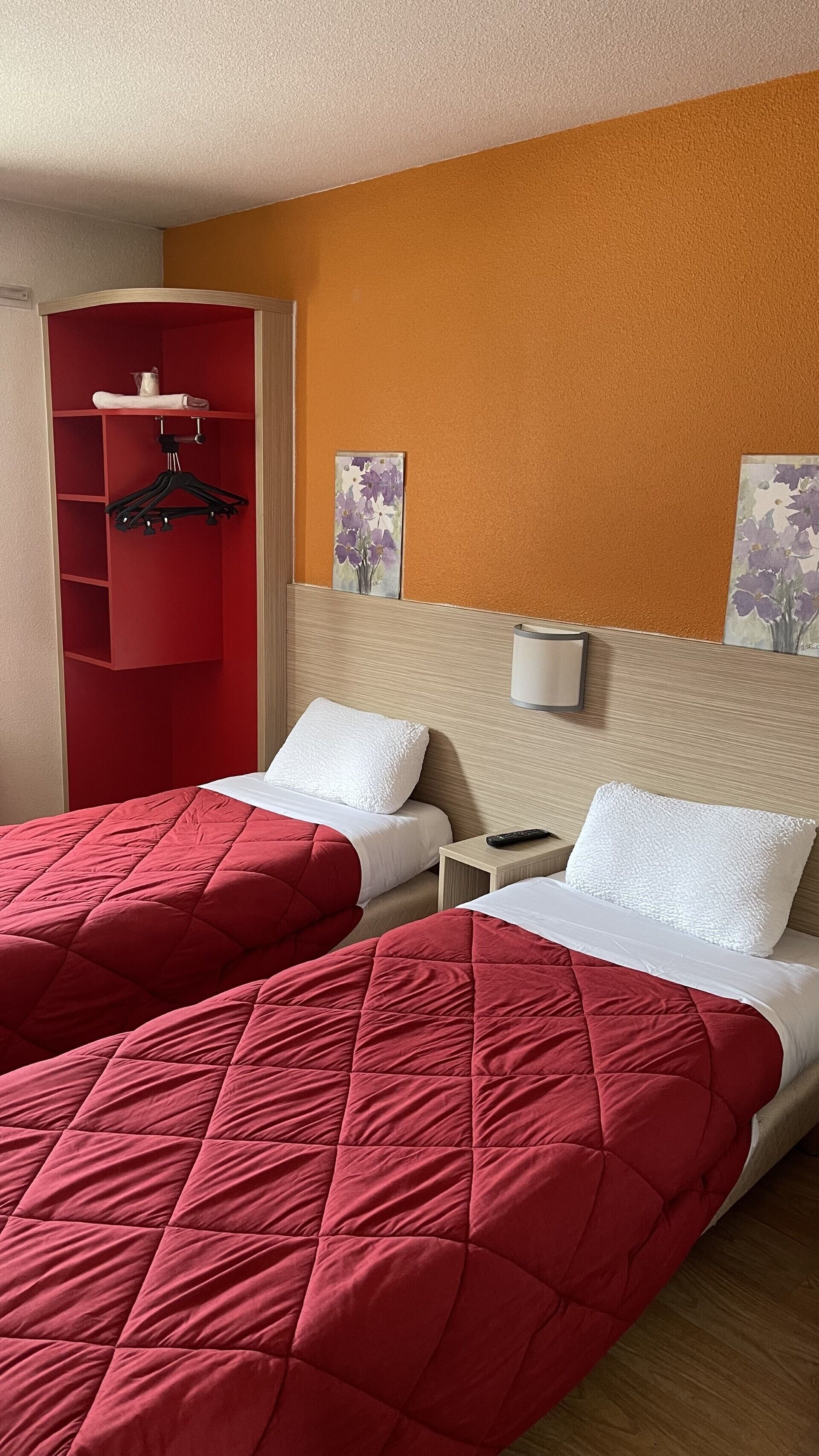 Une chambre d’hôtel avec deux lits, une armoire rouge et un tableau au mur.
