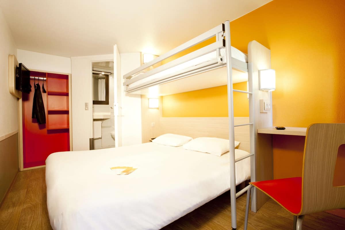 A bunk bed with a desk and chair, a red coat rack, and a bathroom visible through an open door.