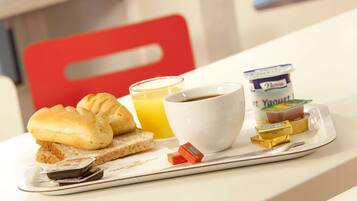 A breakfast tray with toast, croissants, a glass of orange juice, a cup of coffee, a container of yogurt, and a small chocolate bar.