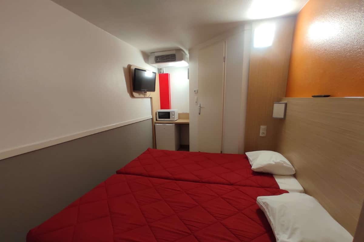 Habitación de hotel con dos camas, televisión, microondas y un escritorio pequeño.
