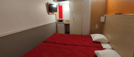 A hotel room with two beds, a television, a microwave, and a small desk.