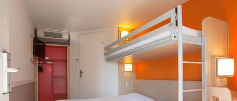 A compact hotel room with a bunk bed, a wardrobe, a bedside lamp, and an air conditioning unit.