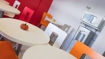 Un comedor moderno con mesas y sillas blancas y anaranjadas, un microondas y una pequeña decoración de calabaza.