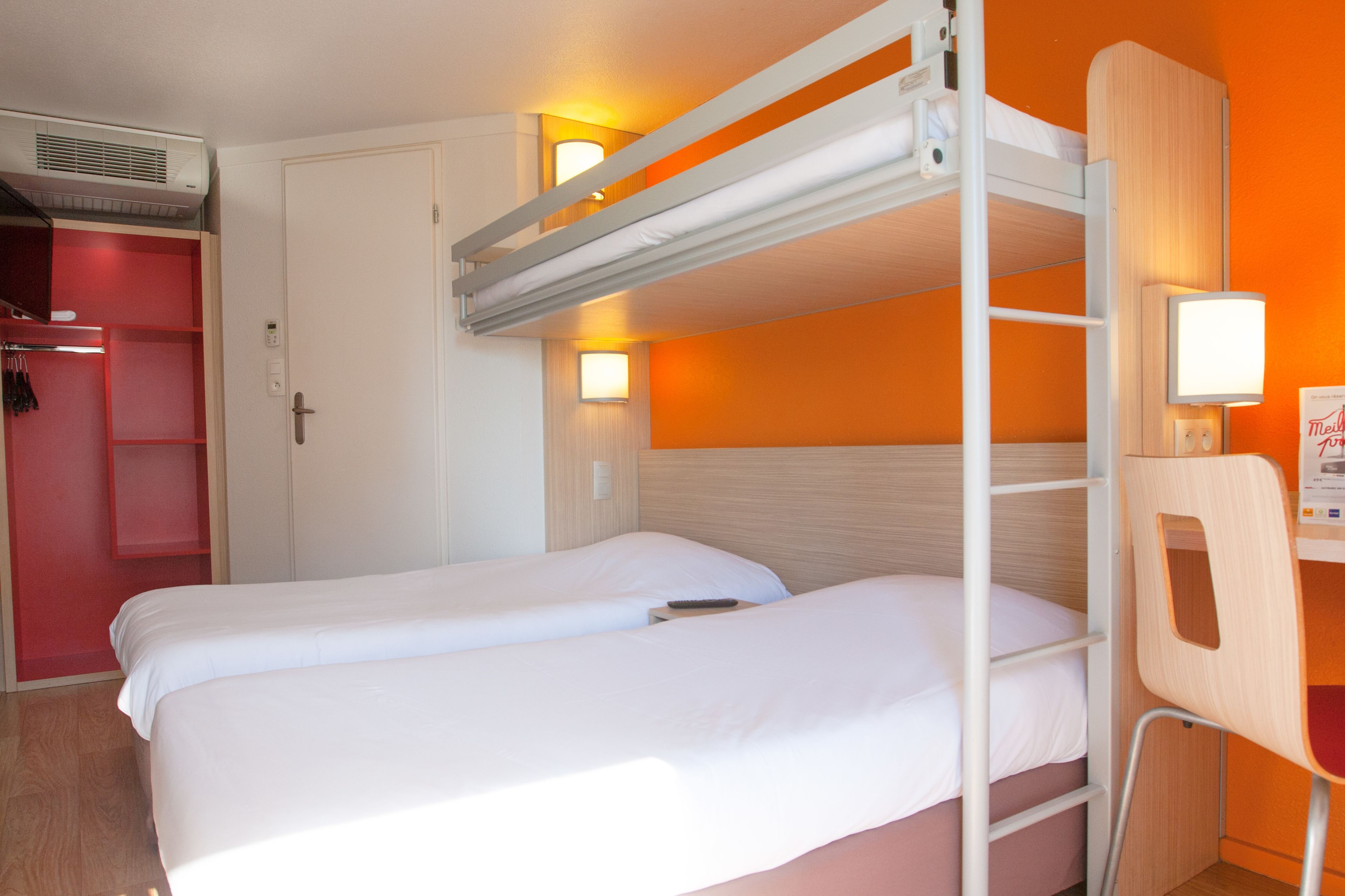 A bunk bed room with a desk and chair, a wardrobe, and a wall-mounted light.