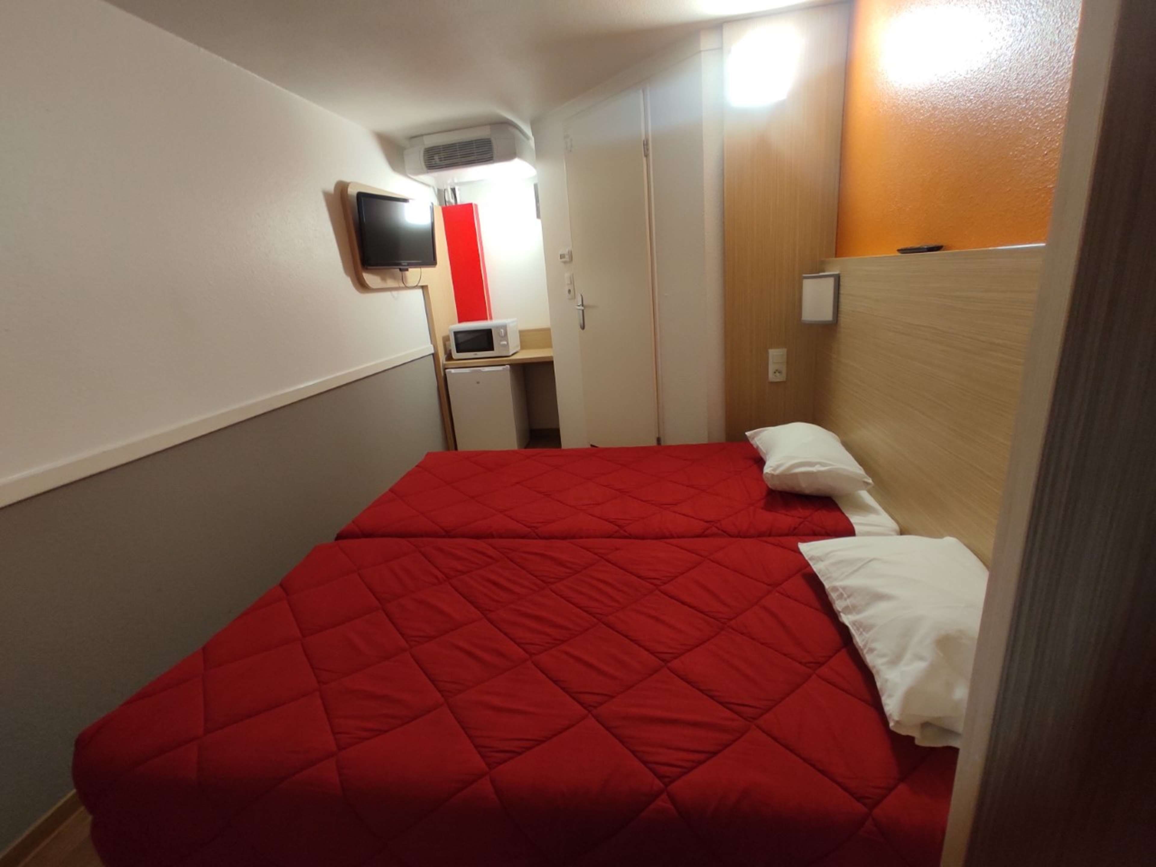 Ein Hotelzimmer mit zwei Betten, einem Fernseher, einer Mikrowelle und einem kleinen Kühlschrank.