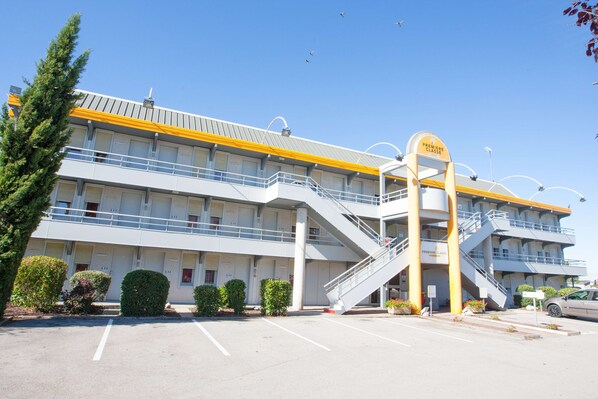 A multi-story hotel with a central staircase, a parking lot, and a clear blue sky. - Première Classe de Dijon Nord - Zénith (Dijon)