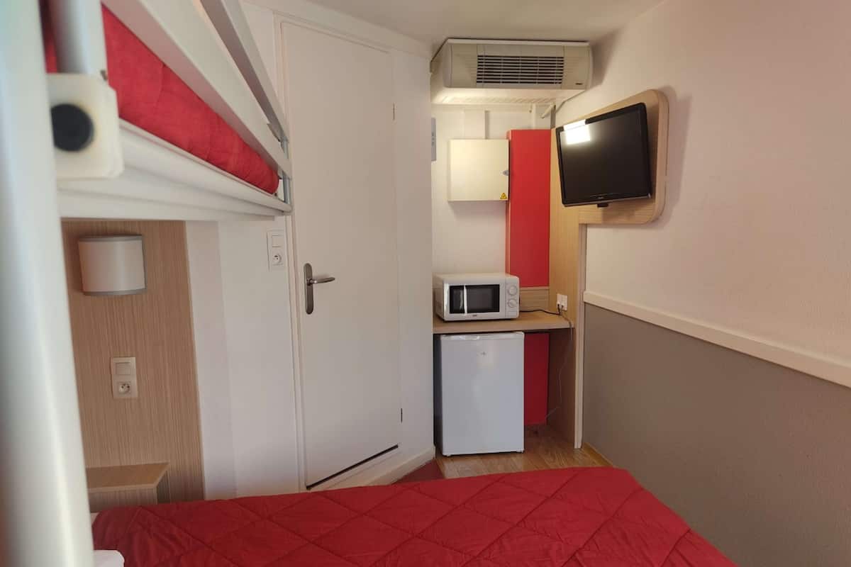 Habitación compacta con una cama, microondas, refrigerador pequeño y televisor montado en la pared.