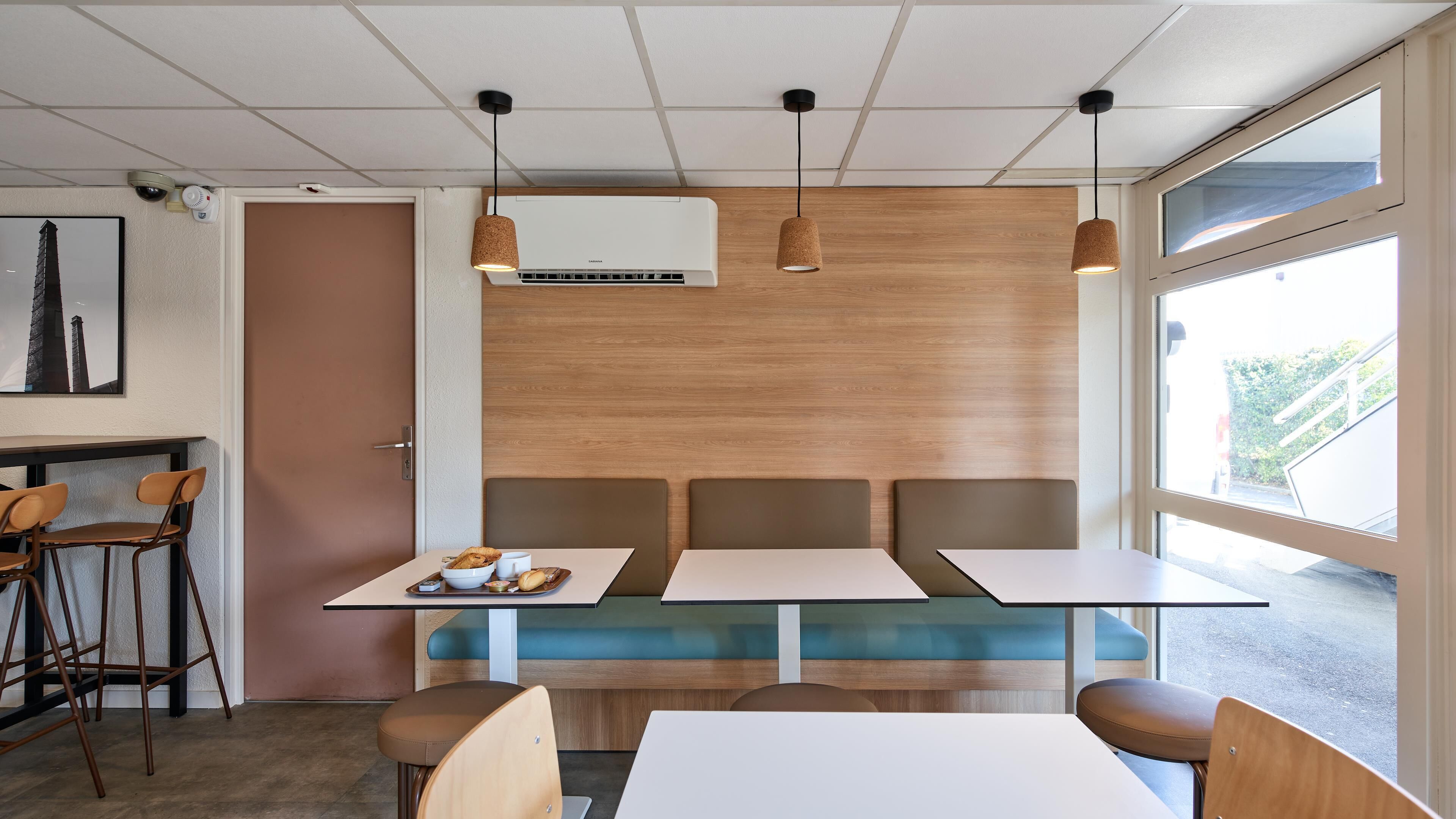 A modern dining area with a high ceiling, pendant lights, a central air conditioning unit, and a view through a large window.
