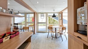 A modern interior with a wooden counter, chairs, a table, and a coffee machine. - Première Classe Valenciennes Ouest - Petite Forêt (Petite-Foret)