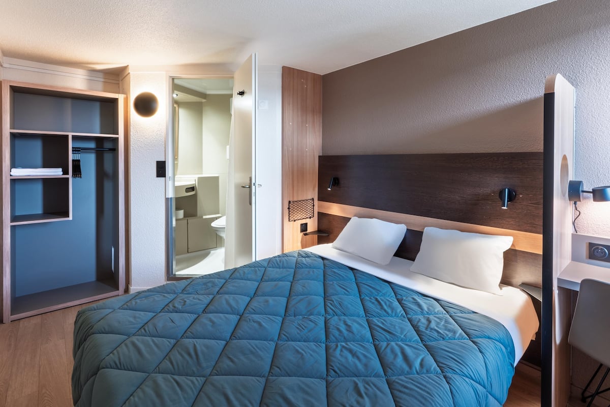 A modern hotel room with a large bed, a walk-in closet, and a bathroom visible through an open door.