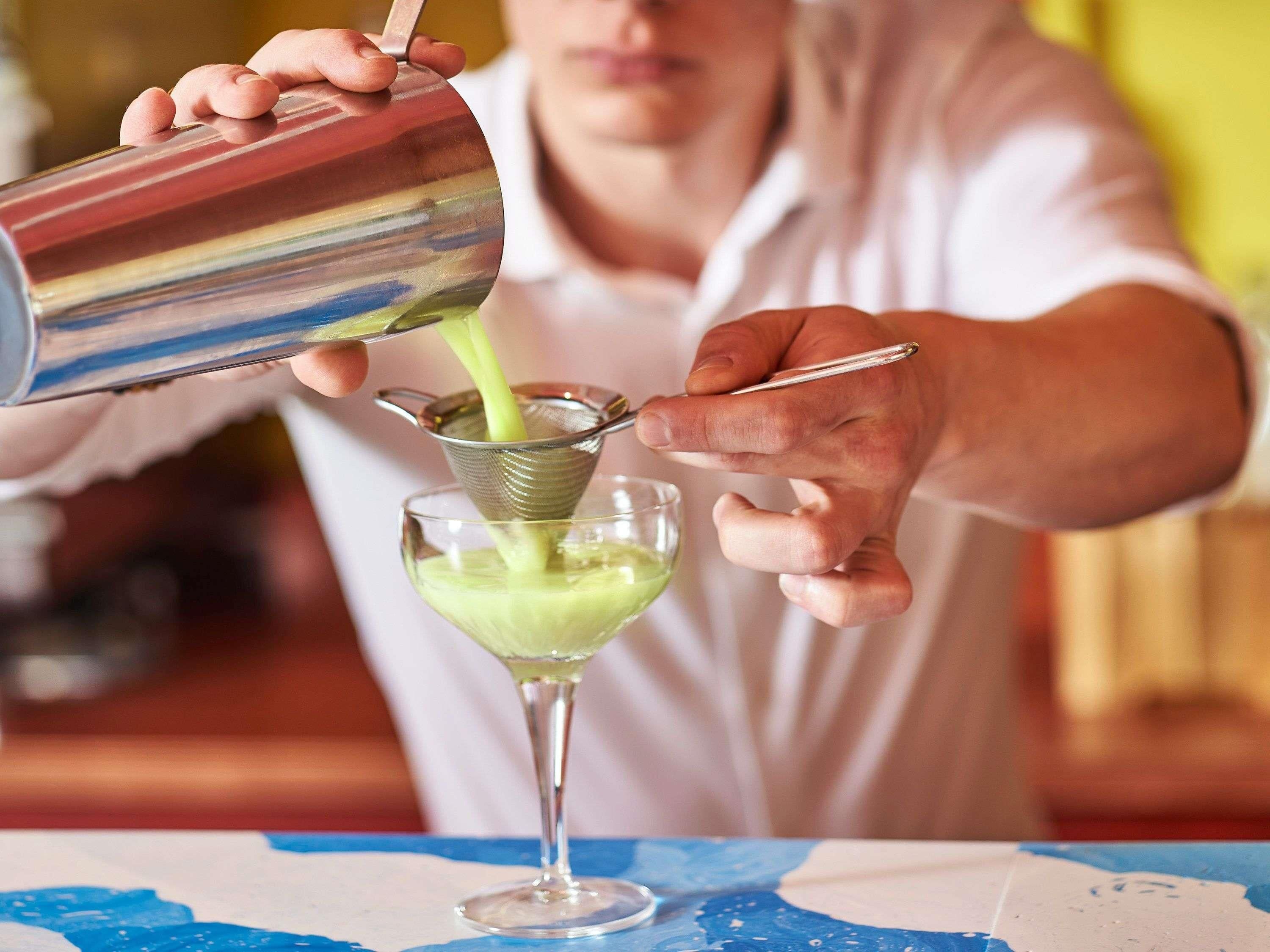 A person pouring a green liquid into a martini glass.