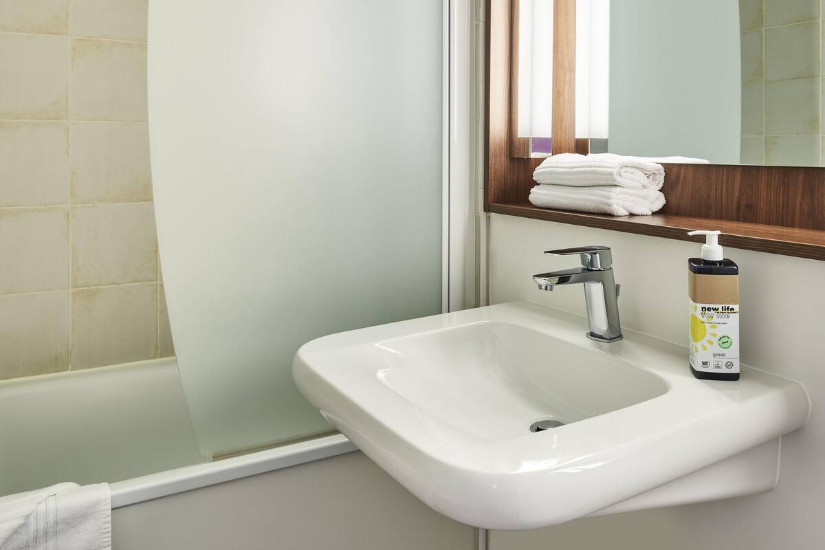 A bathroom with a white sink, a mirror, and a bottle of hand soap.