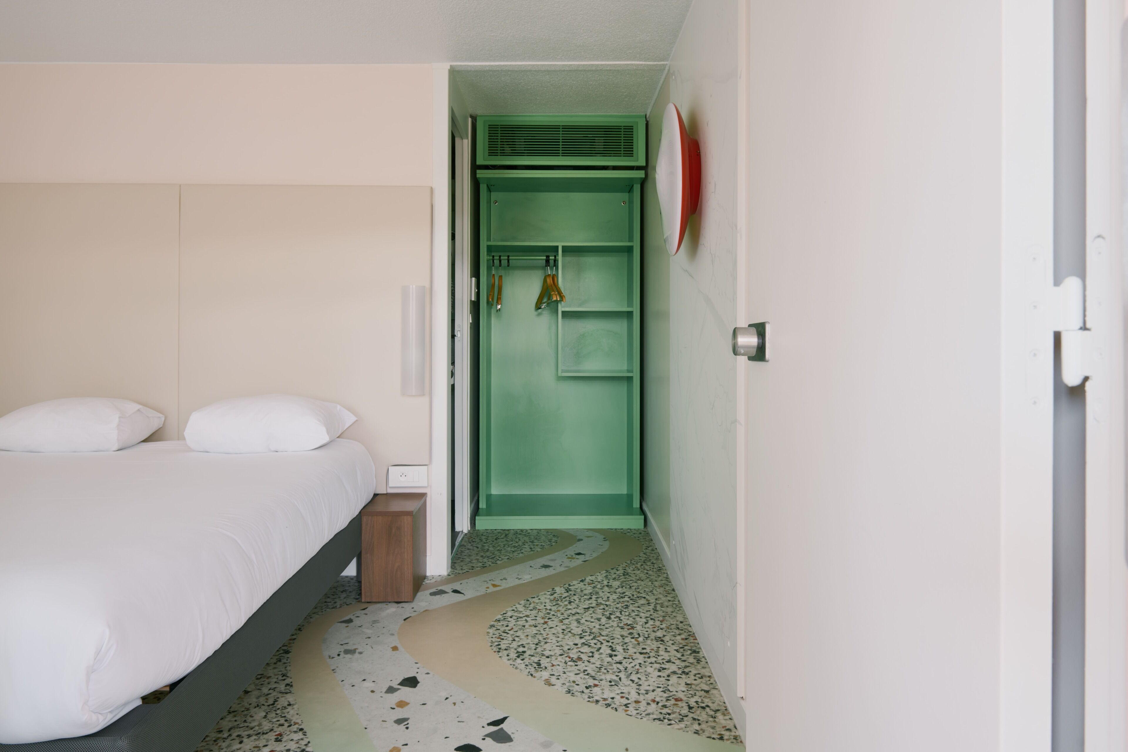 A bedroom with a bed, a green closet, and a white wall.