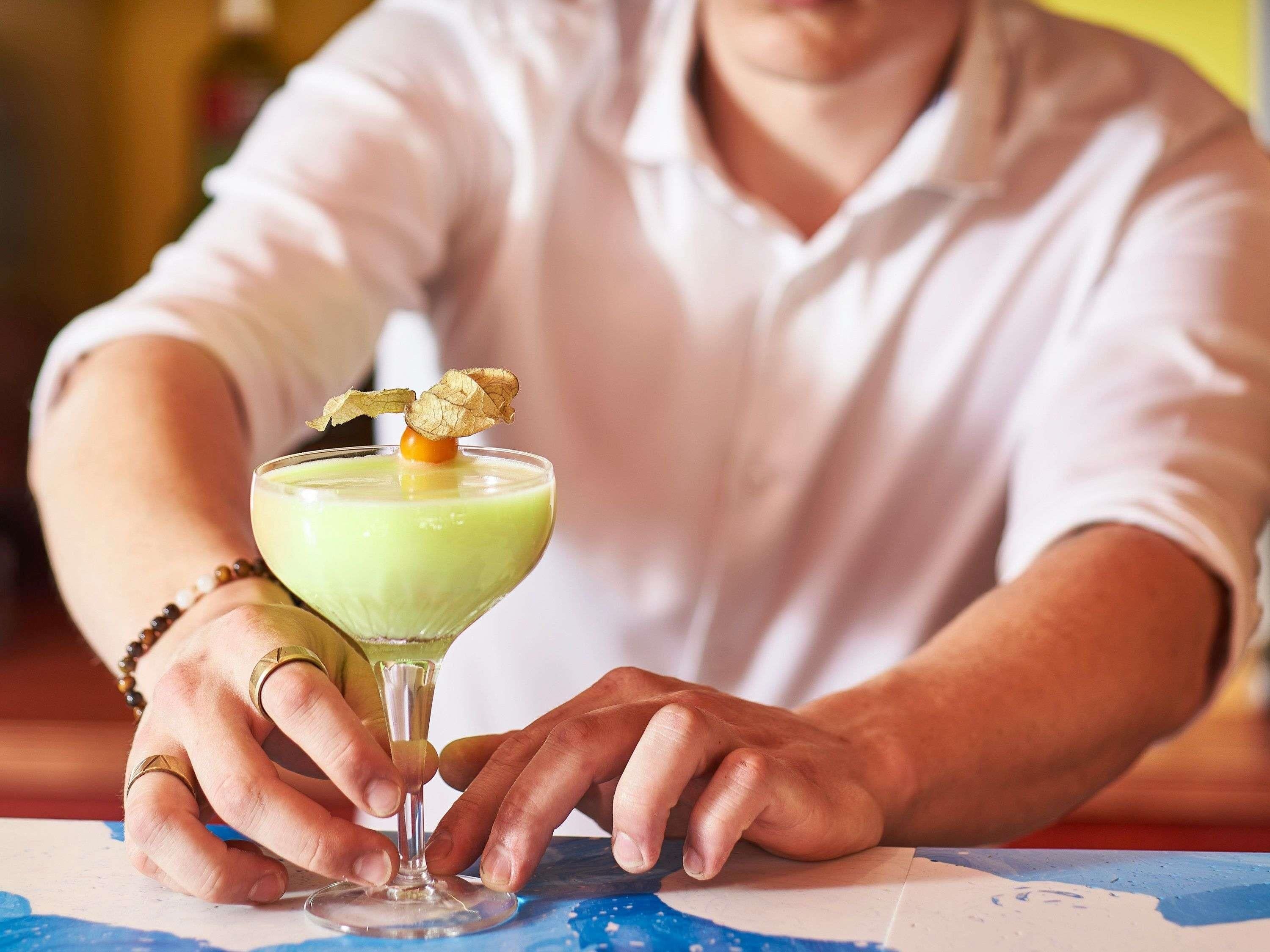 A person holding a cocktail with a garnish, seated at a table with a map.