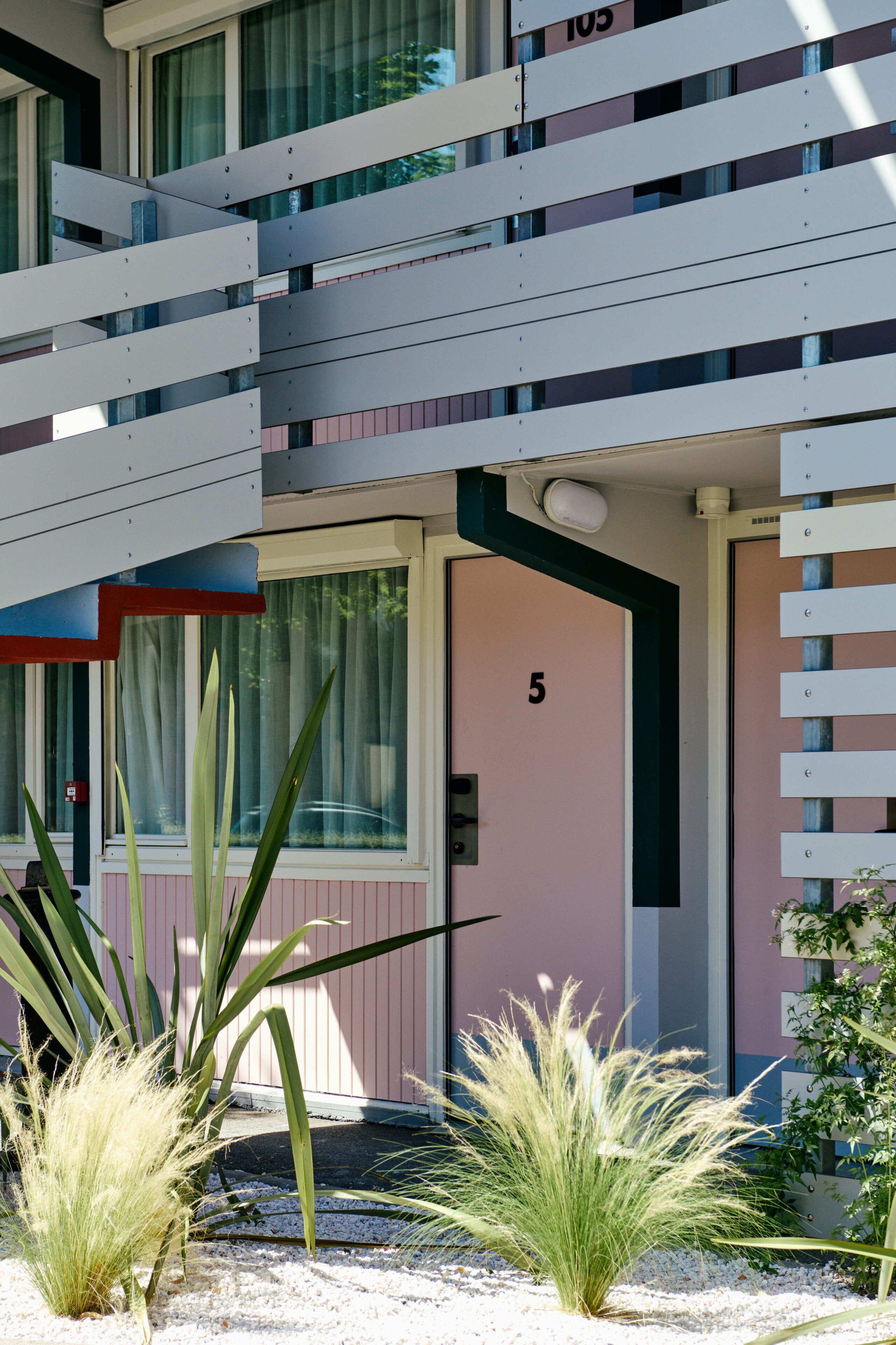 A building with a pink exterior, a balcony with white railings, and a door marked with the number 5.