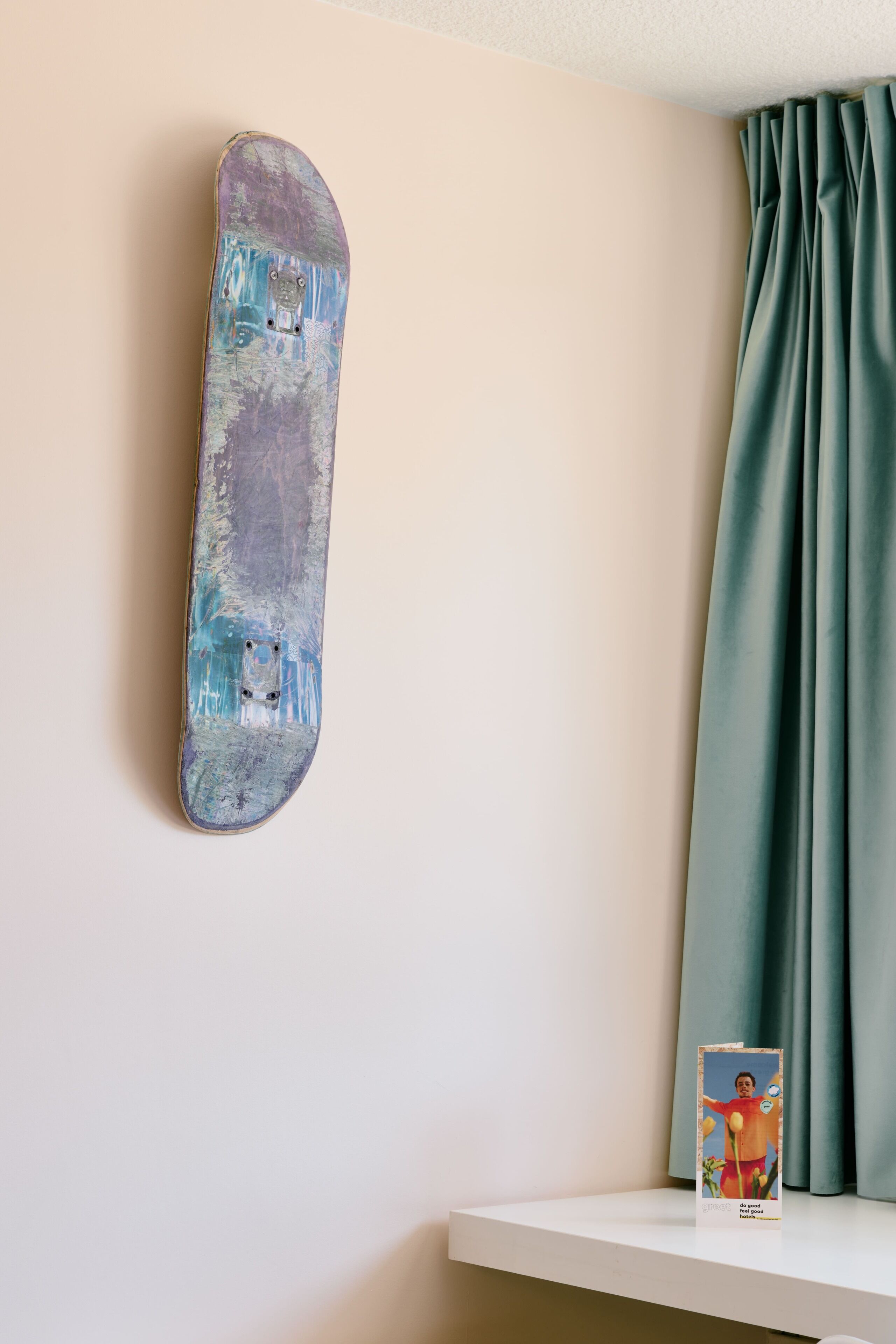 A skateboard leaning against a wall, a green curtain, and a book on a shelf.