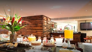 A buffet setup with various food items and a juice dispenser. - Golden Tulip Macaé (Macaé)