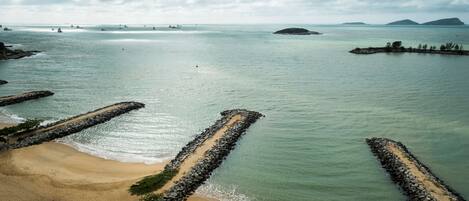 A coastal beach with a rocky breakwater and calm waters.
