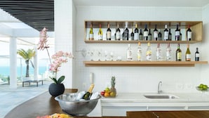 A modern kitchen with a wooden countertop, a wine rack above, and a view of the ocean. - Golden Tulip Macaé (Macaé)