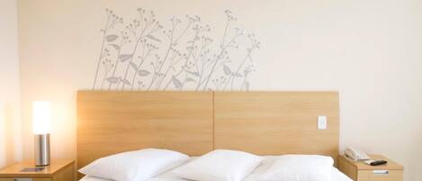 A hotel room with a wooden headboard, a bed with white bedding, two bedside tables, and a wall decoration of flowers.