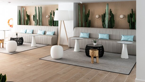 Een moderne woonkamer met een beige bank, twee ronde tafels, en een wand versierd met cactussen.