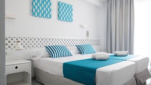 Een tweepersoonsbed met een blauwgroene sprei, twee gestreepte kussens en een witte nachtkastje met een lamp.