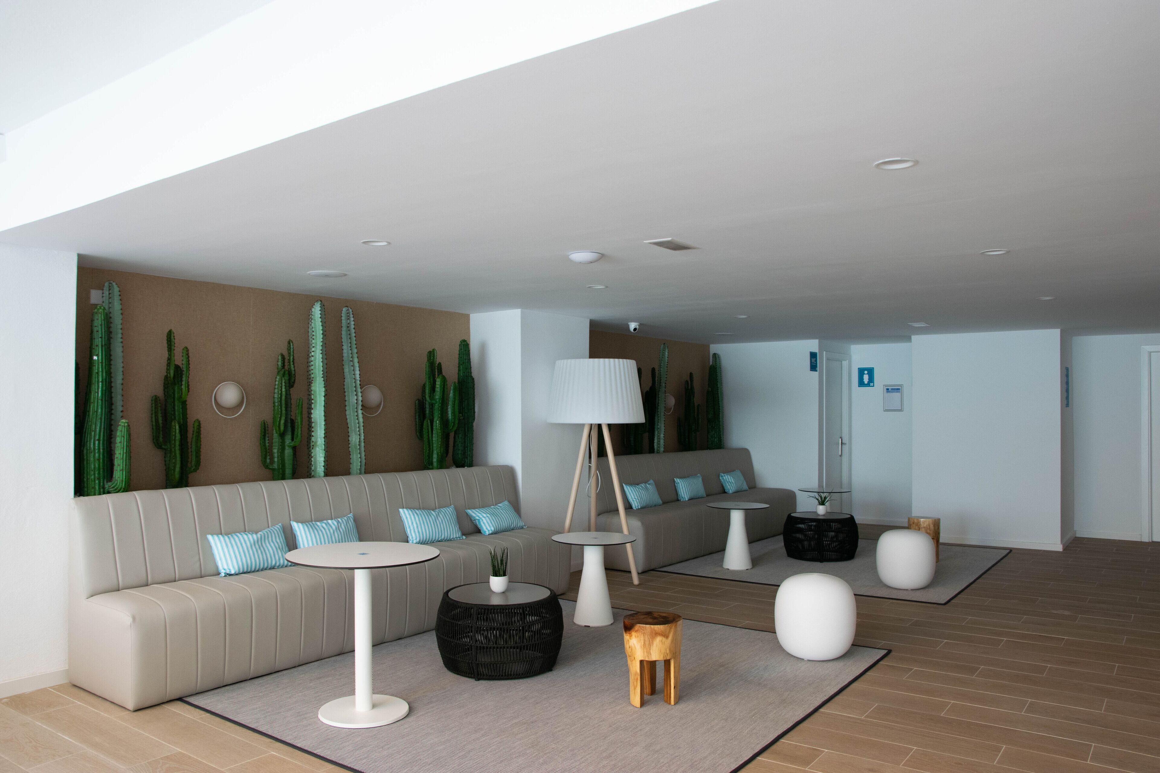 Una sala moderna con un sofá color crema, mesas redondas de centro y una pared decorada con cactus.