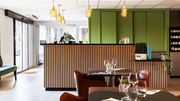 Interior de restaurante con paneles de madera, un mostrador de recepción y una zona de estar con mesas y sillas.