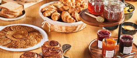 A variety of breads and pastries on a wooden table, including croissants, baguettes, and a loaf of bread.