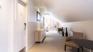 Un pasillo moderno de hotel con un mostrador de recepción, una zona de estar con una mesa y sillas, y una puerta visible con un letrero.