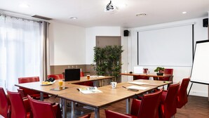 Un salón de conferencias con una larga mesa, sillas rojas, una pantalla de proyector y una planta.