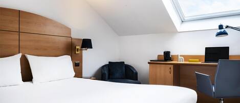 Una habitación de hotel con cama, escritorio, silla, lámpara de escritorio, laptop y ventana con vista al cielo.