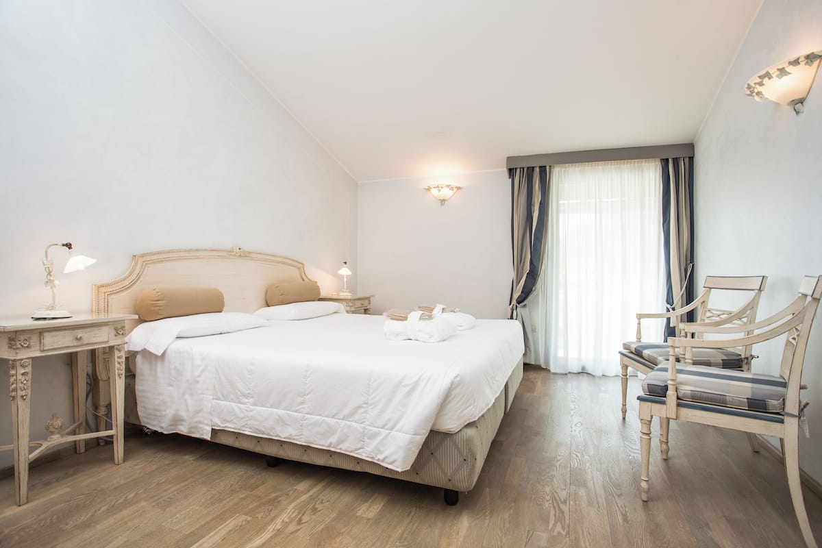 Una camera da letto ordinata con un letto grande, comodini, una sedia e una finestra con tende.