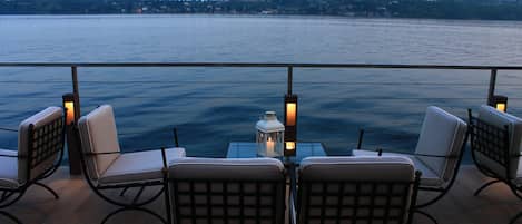 A deck with four chairs and a table, overlooking a body of water with a distant shoreline.