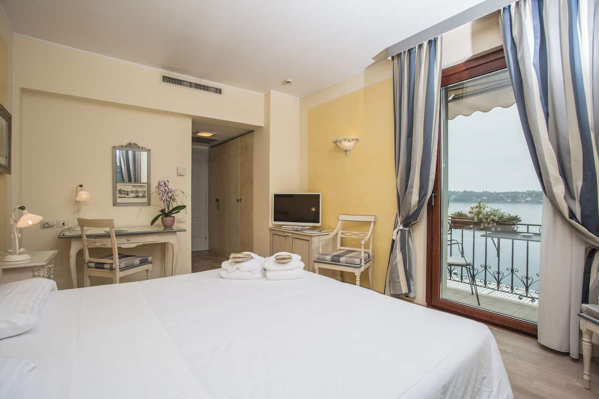 Camera d'albergo con letto, scrivania, sedia, televisore e balcone con vista.